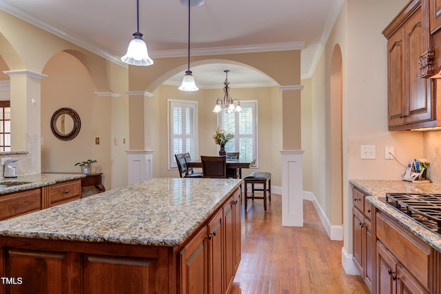 kitchen featuring arched walkways, brown cabinets, ornate columns, and ornamental molding