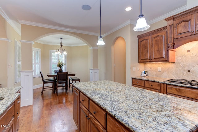 kitchen with gas cooktop, arched walkways, pendant lighting, light stone countertops, and crown molding