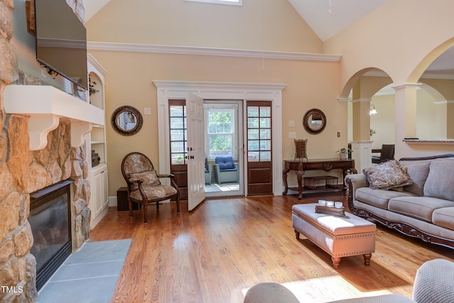 living room featuring ornate columns, high vaulted ceiling, a fireplace with flush hearth, light wood-style flooring, and arched walkways