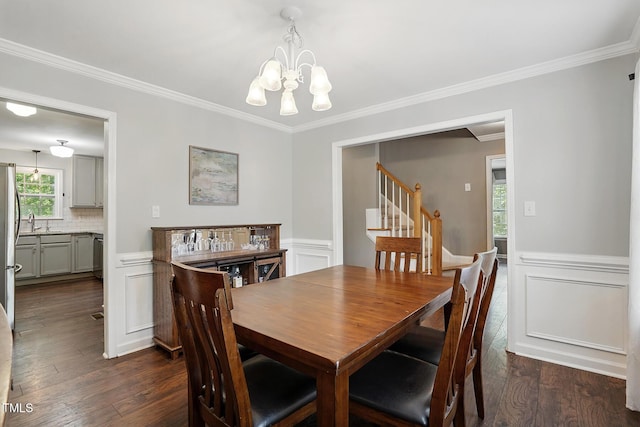 dining room with crown molding, a chandelier, dark wood finished floors, a wainscoted wall, and stairs