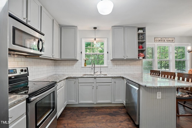 kitchen with stainless steel appliances, a sink, a peninsula, and dark wood-style floors