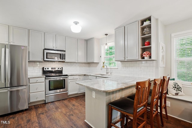 kitchen featuring stainless steel appliances, a sink, open shelves, a peninsula, and dark wood finished floors