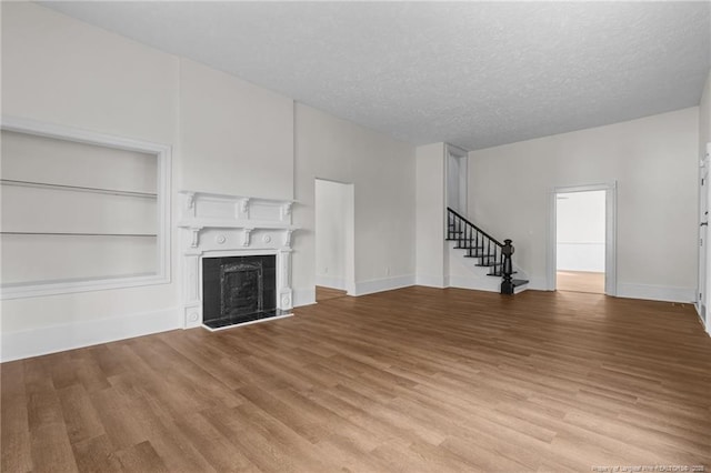 unfurnished living room featuring a textured ceiling, a fireplace, built in shelves, light wood-style floors, and stairs