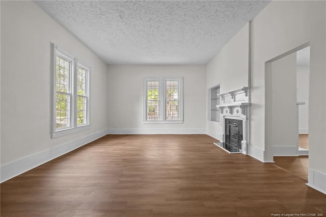 unfurnished living room with baseboards, a textured ceiling, dark wood finished floors, and a fireplace