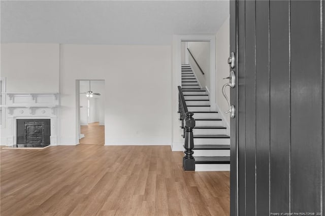 unfurnished living room with ceiling fan, a fireplace, baseboards, stairs, and light wood-style flooring