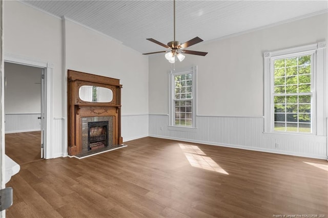 unfurnished living room featuring a ceiling fan, a high end fireplace, crown molding, wood finished floors, and a wainscoted wall