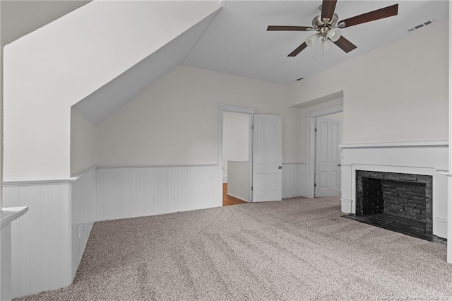 unfurnished living room featuring a ceiling fan, visible vents, a fireplace with flush hearth, wainscoting, and carpet flooring