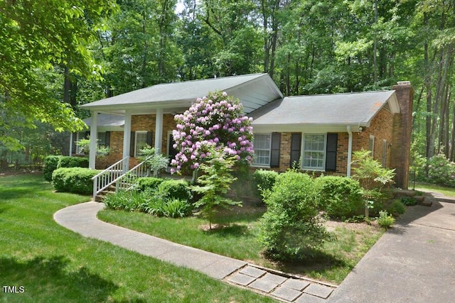 view of front of home featuring covered porch, a chimney, a front lawn, and brick siding