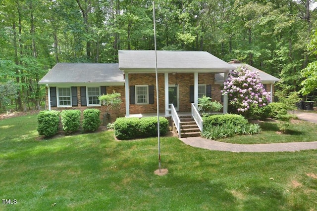 view of front facade with covered porch, brick siding, a forest view, and a front yard
