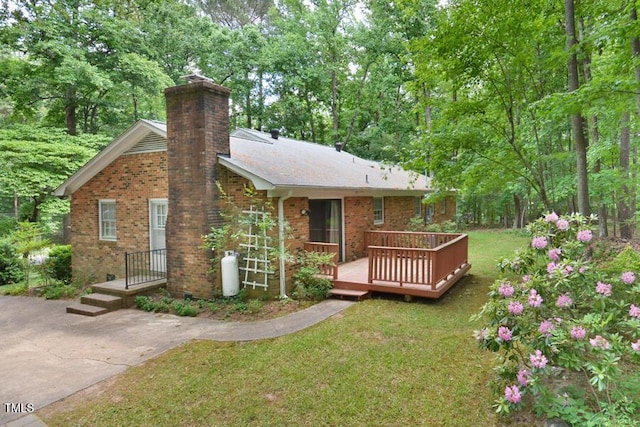 back of house with a lawn, a wooden deck, a chimney, and brick siding