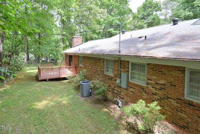 exterior space with a yard, brick siding, a wooden deck, and a chimney