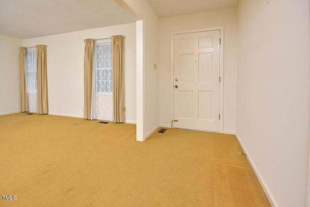 empty room featuring baseboards, visible vents, and light carpet