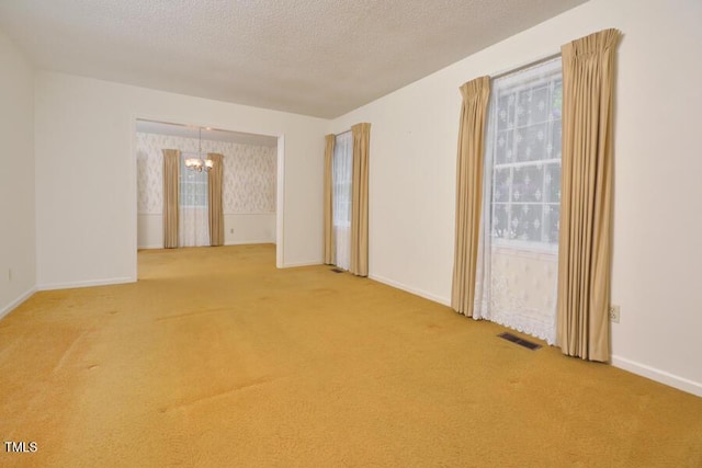 unfurnished room with an inviting chandelier, carpet flooring, baseboards, and visible vents