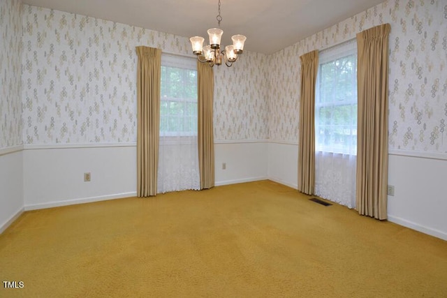 empty room featuring carpet flooring, wallpapered walls, a chandelier, and visible vents