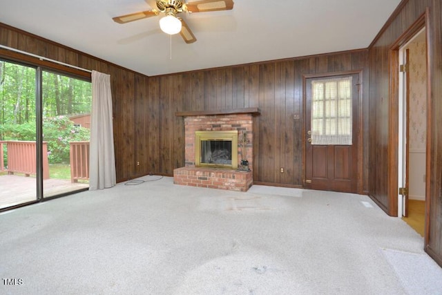 unfurnished living room with carpet flooring, wooden walls, plenty of natural light, and a brick fireplace