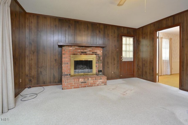 unfurnished living room featuring wooden walls, a ceiling fan, a fireplace, and carpet flooring