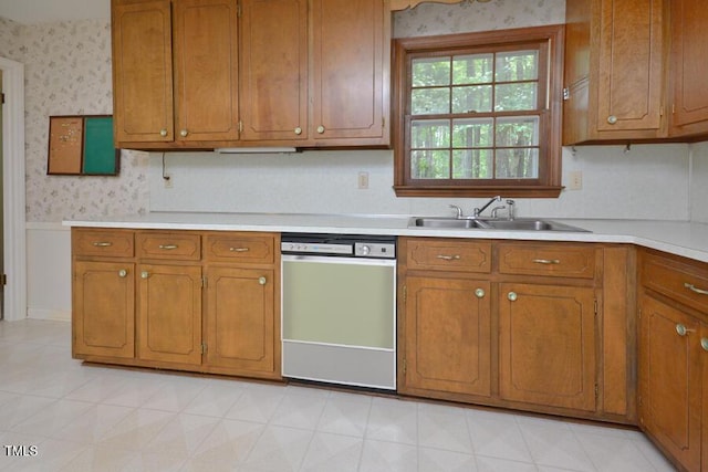 kitchen with light countertops, a sink, dishwasher, and wallpapered walls