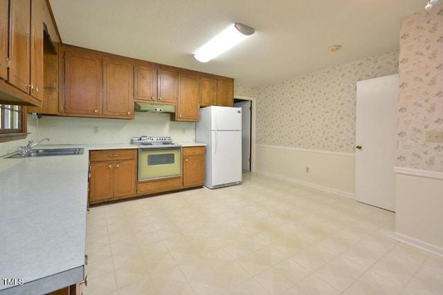 kitchen with brown cabinets, a sink, light countertops, freestanding refrigerator, and under cabinet range hood