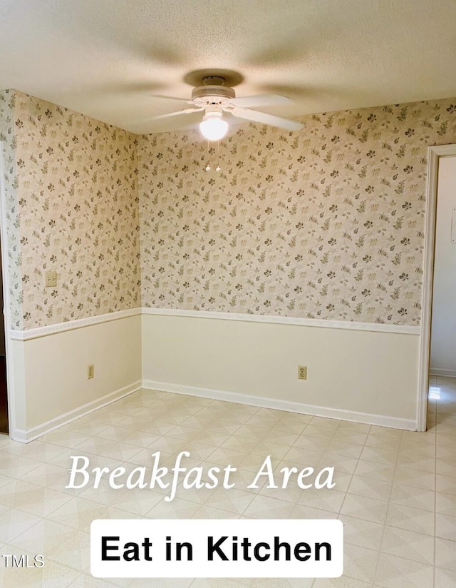 empty room featuring ceiling fan, wainscoting, and wallpapered walls