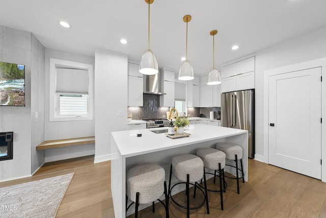 kitchen with light countertops, light wood finished floors, high quality fridge, and an island with sink