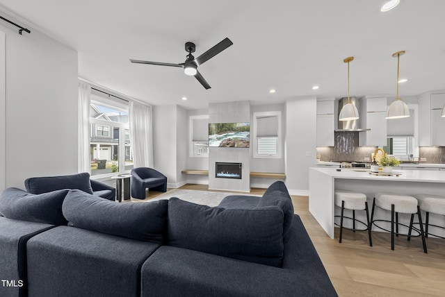 living area featuring recessed lighting, ceiling fan, a large fireplace, and light wood-style floors