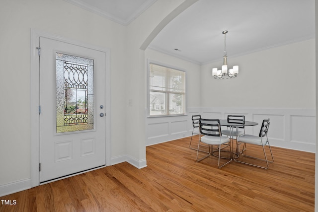foyer with crown molding, arched walkways, light wood finished floors, and a wainscoted wall
