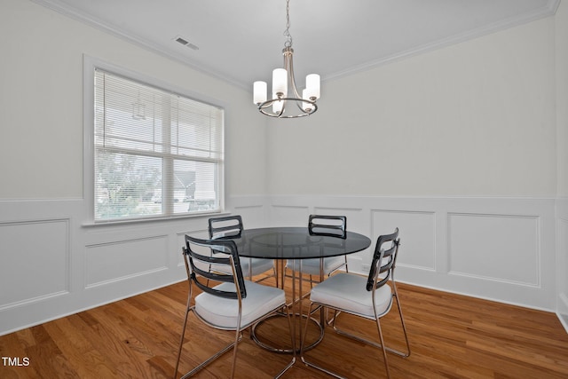 dining space with visible vents, wood finished floors, a wainscoted wall, an inviting chandelier, and ornamental molding
