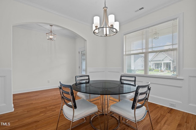 dining area featuring crown molding, wainscoting, wood finished floors, a chandelier, and arched walkways