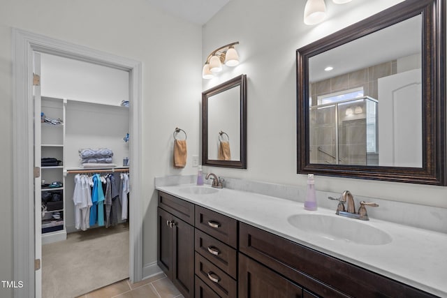 full bathroom with double vanity, a sink, a walk in closet, and a tile shower