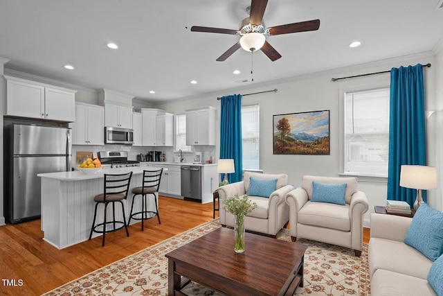 living room featuring light wood-style floors, crown molding, a ceiling fan, and recessed lighting