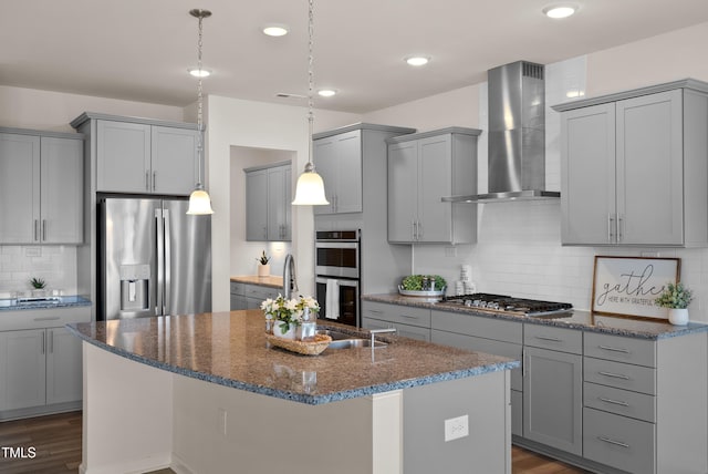 kitchen featuring backsplash, appliances with stainless steel finishes, gray cabinetry, dark stone counters, and wall chimney exhaust hood