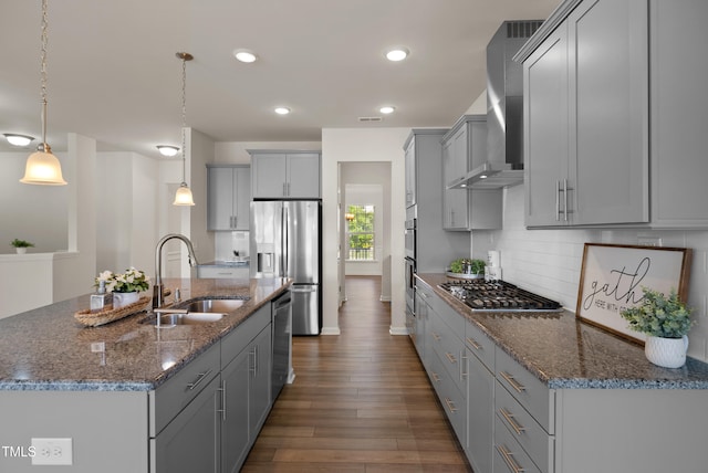 kitchen featuring wall chimney range hood, appliances with stainless steel finishes, dark wood finished floors, a sink, and gray cabinetry