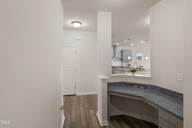 corridor featuring baseboards, a sink, and wood finished floors