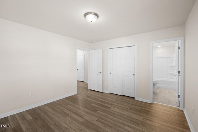 unfurnished bedroom with baseboards, wood finished floors, ensuite bathroom, and a closet