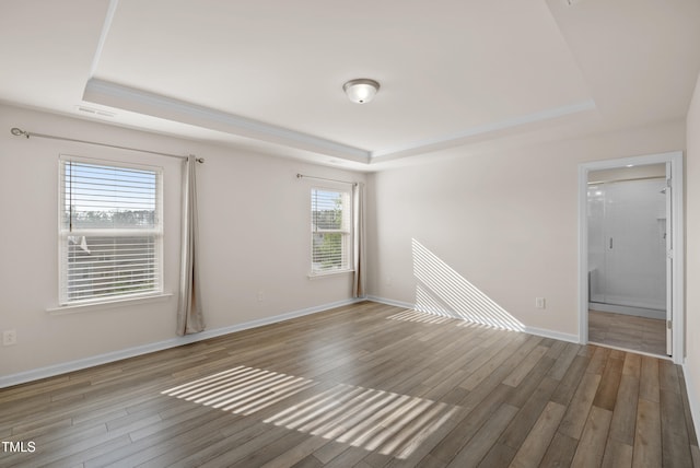 empty room with a raised ceiling, baseboards, and wood finished floors
