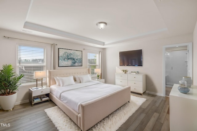bedroom featuring baseboards, a tray ceiling, and light wood-style flooring