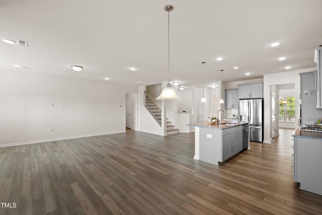 kitchen with open floor plan, a center island with sink, gray cabinets, a sink, and stainless steel appliances