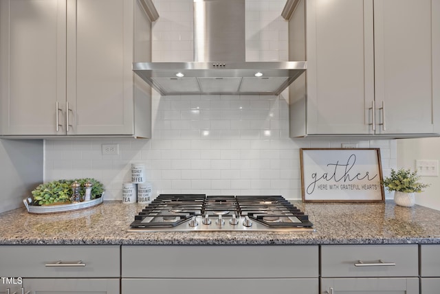 kitchen with wall chimney range hood, gray cabinetry, stainless steel gas cooktop, and backsplash