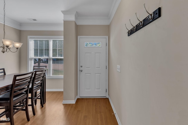 foyer entrance with visible vents, wood finished floors, baseboards, a notable chandelier, and ornamental molding