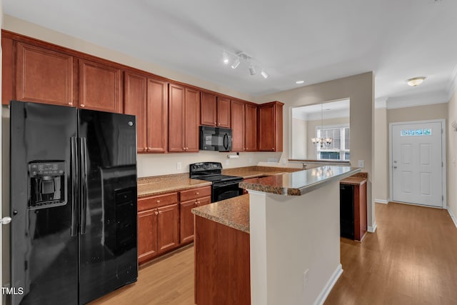 kitchen featuring brown cabinets, black appliances, a peninsula, light wood finished floors, and a chandelier