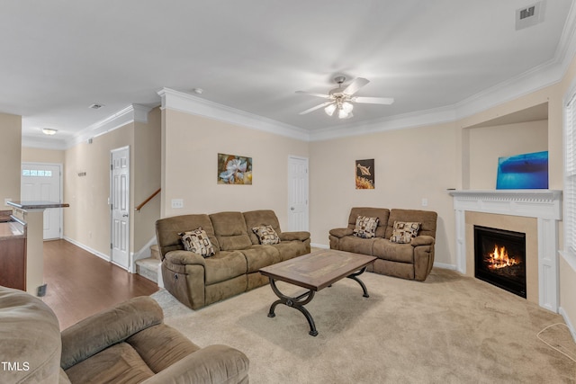 living room with a ceiling fan, visible vents, baseboards, a warm lit fireplace, and ornamental molding