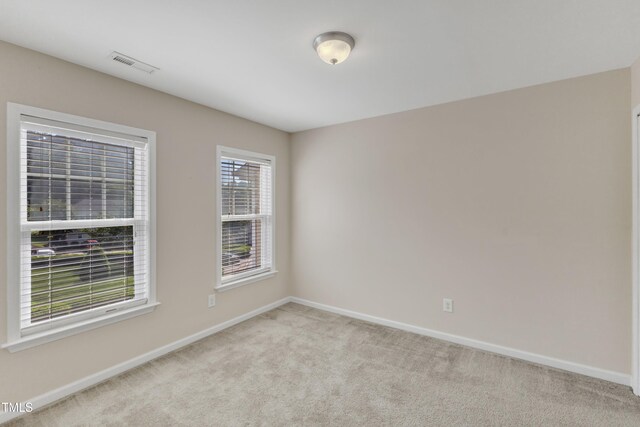 spare room featuring baseboards, light colored carpet, and visible vents