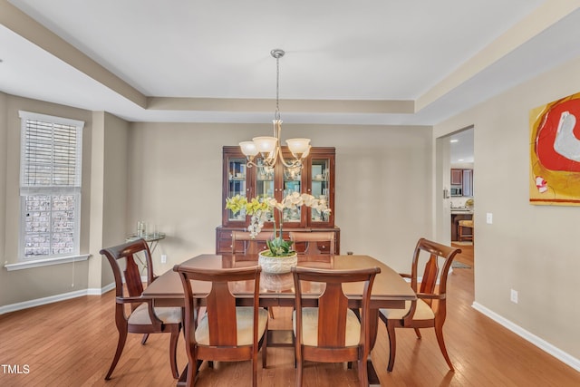 dining room featuring hardwood / wood-style flooring, a raised ceiling, a chandelier, and baseboards