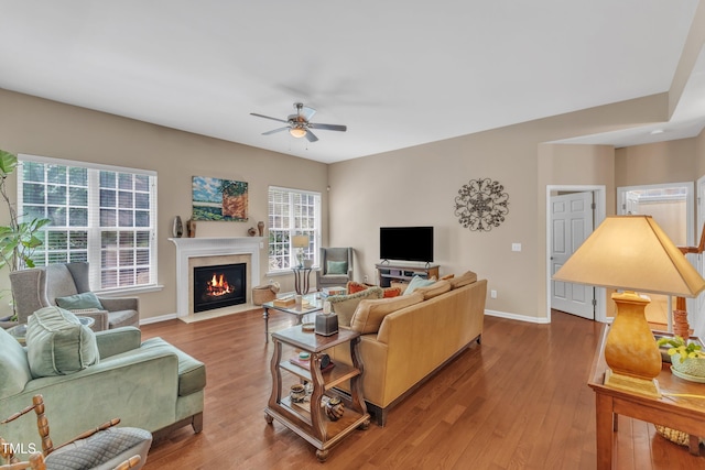living area featuring a ceiling fan, plenty of natural light, a fireplace with flush hearth, and baseboards