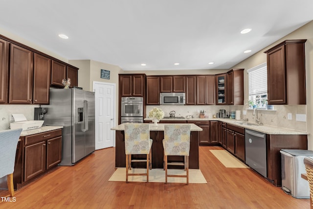kitchen with stainless steel appliances, a sink, a kitchen island, a breakfast bar, and tasteful backsplash