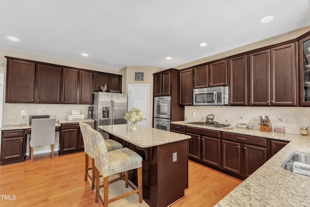 kitchen featuring stainless steel appliances, dark brown cabinets, a kitchen bar, tasteful backsplash, and recessed lighting