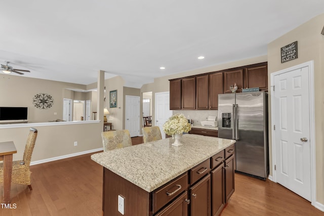 kitchen featuring stainless steel refrigerator with ice dispenser, open floor plan, wood finished floors, a ceiling fan, and baseboards