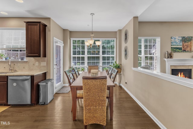 dining space with a chandelier, wood-type flooring, baseboards, and a lit fireplace