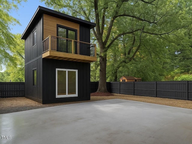 back of house with board and batten siding, a fenced backyard, a balcony, and a patio area