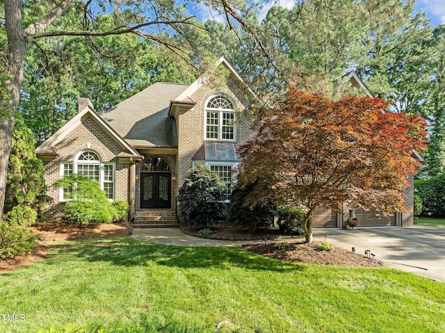 view of front facade with french doors, brick siding, a front yard, a garage, and driveway